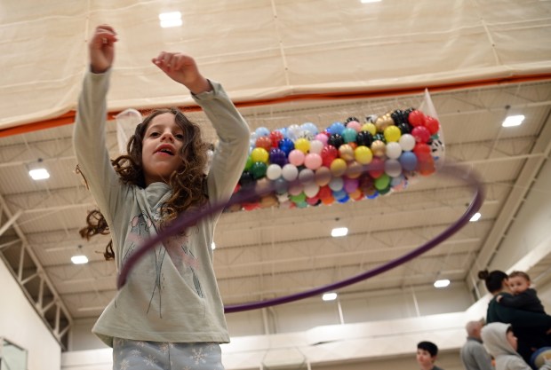 The 250 balloons are in a net on the ceiling, waiting to be dropped at a noon countdown. Trying the Hula hoop is Alma Slivnick, 6, a kindergartner from Deerfield, at Noon Year's Eve on Dec. 31, 2024 in Deerfield at Sachs Recreation Center. (Karie Angell Luc/Pioneer Press)