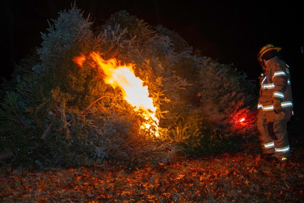 An Ogden Dunes firefighter sets a pile of Christmas trees alight using a flare during a Twelfth Night celebration in Ogden Dunes on Monday, Jan. 6, 2025. (Michael Gard/for the Post-Tribune)