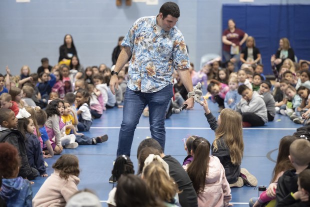 River Forest graduate, teacher, and author of children's book "The Little Elephant Who Couldn't Sit Still", Allen Long, holds his arm out so an Evans Elementary student can touch a plush elephant on his wrist, as he speaks about his book to the school on Monday, April 10, 2023. (Kyle Telechan for the Post-Tribune)