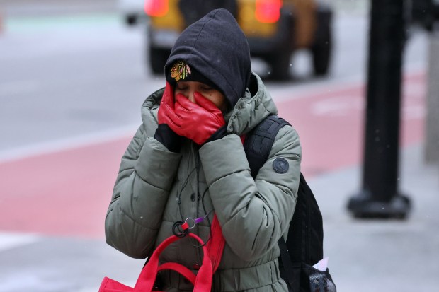 A pedestrian at Dearborn Street and Jackson Boulevard in Chicago covers her face as the wind chill makes it feel like 10 degrees on Feb. 11, 2025. (Terrence Antonio James/Chicago Tribune)