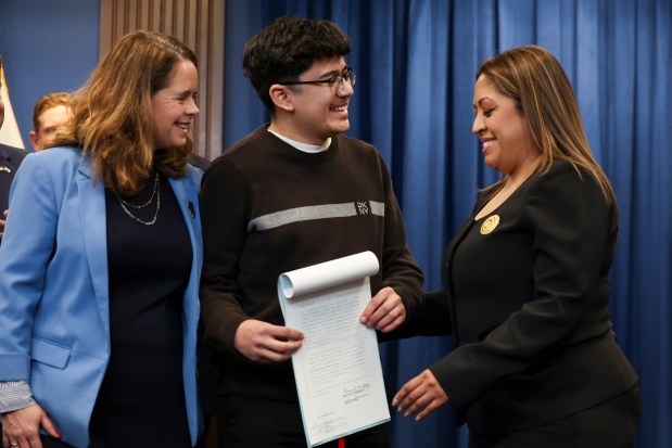 Manny Alvarez, Karina Gonzalez's son, center, smiles as he stands with bill sponsors State Rep. Maura Hirschauer, left, and State Sen. Celina Villanueva, after Gov. JB Pritzker signed "Karina's Law" to strengthen protections for survivors of domestic violence at the State of Illinois building on Feb. 10, 2025. (Eileen T. Meslar/Chicago Tribune)