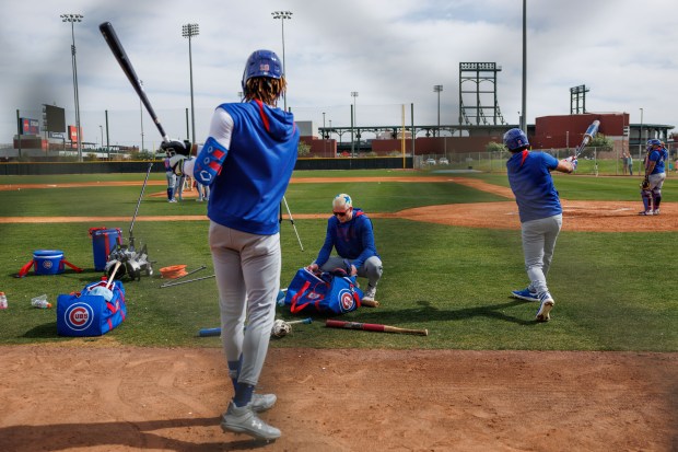 Cubs outfielder Kevin Alcántara, left, and infielder Nicky Lopez warm up on the side of a practice field while center fielder Pete Crow-Armstrong kneels over his bag at live batting practice during spring training on Feb. 13, 2025, at Sloan Park in Mesa, Ariz. (Armando L. Sanchez/Chicago Tribune)