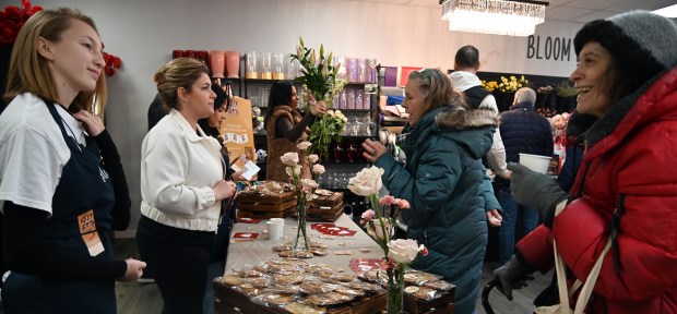 Center, Sylvia Salimi of Long Grove, owner of Blooming Boutique Flowers, a business storefront which opened in May of 2024, carries flowers to the register counter. Second from left, staffing an outreach table is Hana Weber of Long Grove, operator of Sorelle Italian Market, which opened in Aug. of 2024 in Long Grove. Taken during the Cocoa Crawl in downtown Long Grove on Feb. 8, 2025. (Karie Angell Luc/Lake County News-Sun)