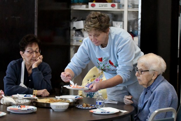 Olga Yanisheuska, center, adds sour cream to her plate of pierogis as Neva Lenhart, left, and Stephanie Babij wait their turn at the St. Josaphat Ukrainian Catholic Church in Munster, Indiana on Friday, Feb. 21, 2025. The women were part of a volunteer crew making perogies earlier in the morning. (Andy Lavalley for the Post-Tribune)