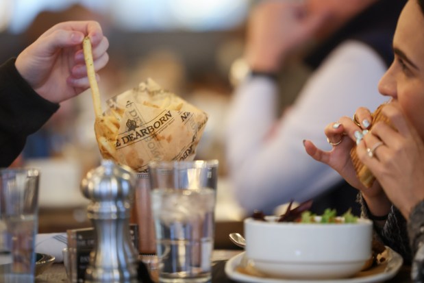 Manuela Pinilla, of Trauma Lawyers, right, bites into the cuban panini, while her friend, Spencer Hamilton, grabs a french fry during their lunch break Chicagoans at The Dearborn in Chicago on Feb. 12, 2025. (Audrey Richardson/Chicago Tribune)