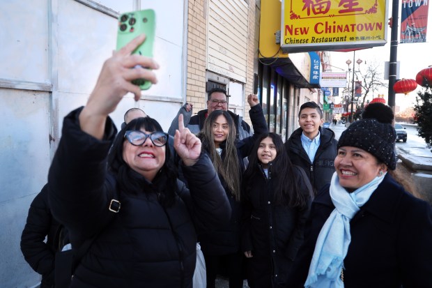 Julie Contreras, from left, of the group United Giving Hope, records a video to post on social media with Briseida de la Cruz Morales, arm raised, and her children Edith Sanchez de la Cruz and Christian Sanchez de la Cruz in Chicago's Chinatown after the family appeared before an immigration court judge on Feb. 13, 2025. The judge allowed them to remain in the United States and said their next court appearance would be in 2028. (Terrence Antonio James/Chicago Tribune)