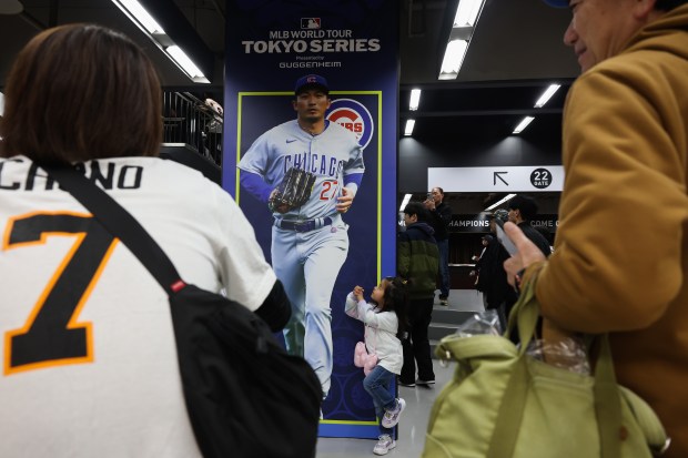 A child makes a batting stance pose next to a poster of Chicago Cubs outfielder Seiya Suzuki while being photographed by her father before an exhibition game between the Cubs and Yomiuri Giants at the Tokyo Dome on March 16, 2025, in Tokyo. (John J. Kim/Chicago Tribune)