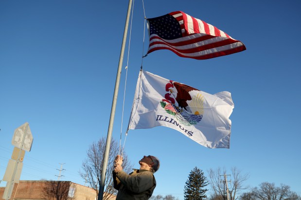 Sales associate Tom Koenig raises the U.S. and Illinois flags outside an Ace Hardware store as it opens on Jan. 27, 2025, in LaGrange Park. (Antonio Perez/Chicago Tribune)