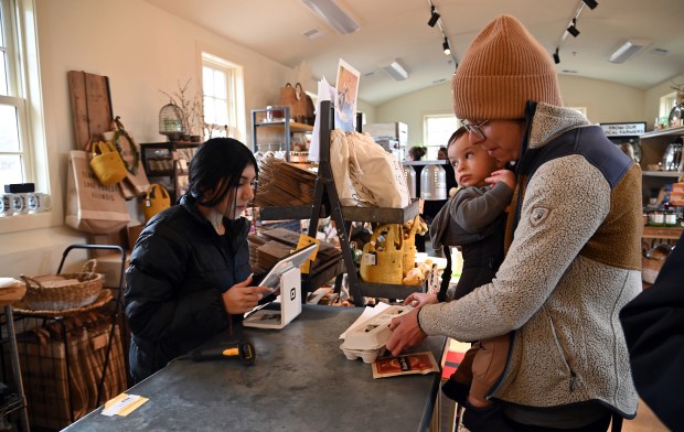 Left, intern Aneth Castillo of Waukegan, 17, a senior at Cristo Rey St. Martin College Prep of Waukegan, checks out eggs for customer Jane Ulitskaya of Northbrook, holding son Andre Katz, 20 months, at the Elawa Farm Winter Market in Lake Forest on March 7, 2025. (Karie Angell Luc/Lake County News Sun)