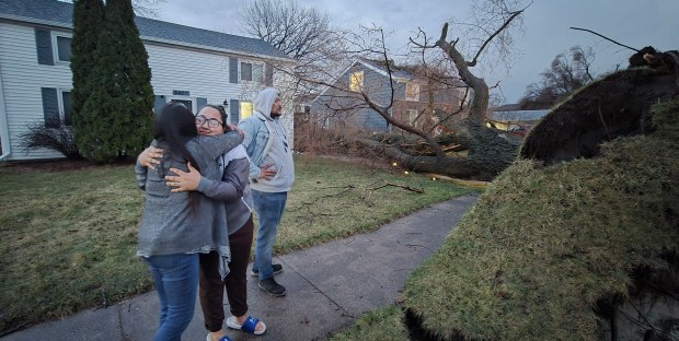 Jessica Ramirez, center, hugs her mom, Rosie Ramirez, while Jessica Ramirez's husband, Joshua Berthiaume, looks at the tree that fell in his driveway after a storm tore down Forrest Drive in Highland Wednesday, March 19, 2025. Rosie Ramirez moved her car out of the driveway seconds before the tree came down. (Michelle L. Quinn/for Post-Tribune)