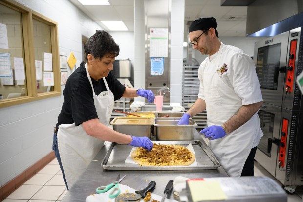 River Forest High School food service director Nick Alessandri, on right, and cook Cathy Doeing top a carnitas pizza with pork sourced from a local farm through the NWI Food Council Farm to School program on Friday, March 21, 2025. (Kyle Telechan/for the Post-Tribune)