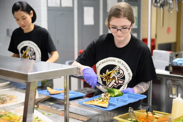 Substitute food service worker Dezerea Carothers plates a serving of broccoli with a slice of carnitas pizza during lunch at River Forest High School on Friday, March 21, 2025. (Kyle Telechan/for the Post-Tribune)