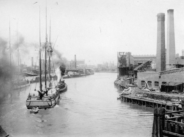 A view of the Chicago River, looking up river from the North Halsted Street Bridge near Goose Island, shows a tugboat towing a schooner with lumberyard, factories, warehouses and grain elevators visible along the banks in Chicago, circa 1893. (Chicago History Musem, ICHi-093188)