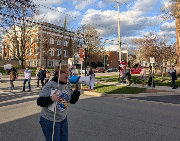 Barbara O'Meara leads a round of chants as protesters march through Naperville Tuesday. (Tess Kenny/Naperville Sun)