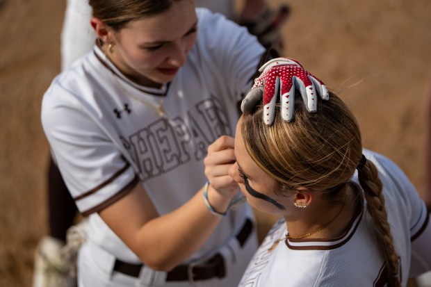 Shepard first baseman Emma Gelecke (5) applies facepaint for teammate and pitcher Kailey Selvage before their game against Argo at Shepard High School in Palos Heights on Monday, April 28, 2025. (Lukas Katilius/for the Daily Southtown)
