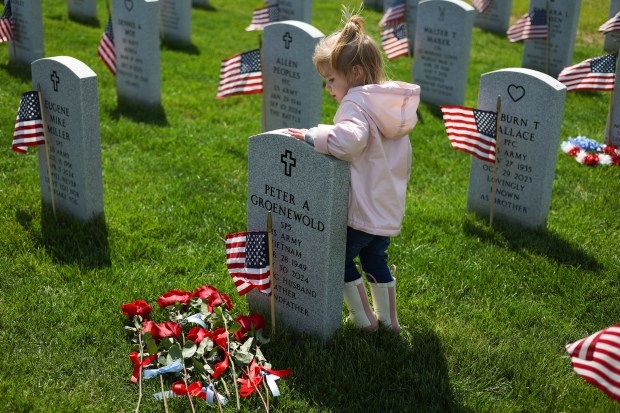 Vivian Barr, 2, places pennies on her grandfather's headstone at Abraham Lincoln National Cemetery during the annual Flags In event, ahead of Memorial Day, on May 23, 2025, in Elwood. Barr, whose grandfather died last year, placed the penny to signify that she visited his grave. (Audrey Richardson/Chicago Tribune)