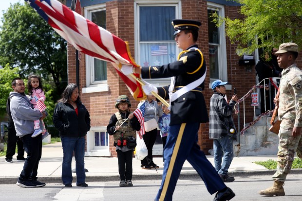 Cameron Vazquez, 9, standing wearing a military costume in background, watches as an honor guard passes during the McKinley Park Memorial Day parade, May 26, 2025. (Antonio Perez/Chicago Tribune)