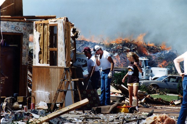 Kevin Smith gets a phone call as his friends and daughter, Amy Sue, 13, help demolish what's left of his home in Plainfield on Aug. 31, 1990, three days after a deadly tornado tore through town. Debris from other buildings burns in the background. (Frank Hanes/Chicago Tribune)