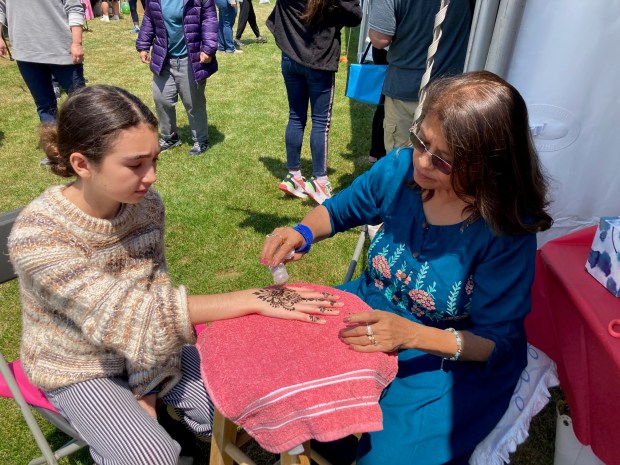 Smita Shah, right, sprinkles silver glitter over the henna design she has just applied to the hand of Yana Williams at the 2023 Skokie Festival of Cultures. (Pam DeFiglio/Chicago Tribune)