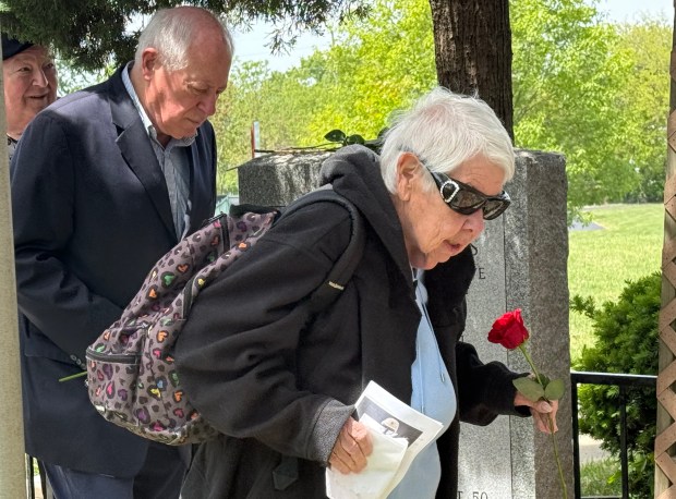Judy Kissel, of Palos Heights, is escorted by former Gov. Pat Quinn as she presents a rose at a monument during Memorial Day ceremonies May 26, 2025, at Blue Island's Memorial Park. (Jeff Vorva/for the Daily Southtown)