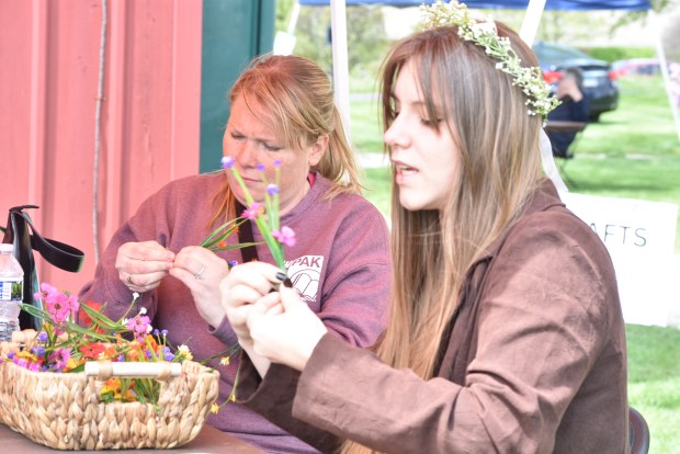 Emily Kurtis, left, and Phoenix Crane make flower garlands at a craft table before the maypole dance May 4, 2025, in Orland Park. (Jesse Wright/for the Daily Southtown)