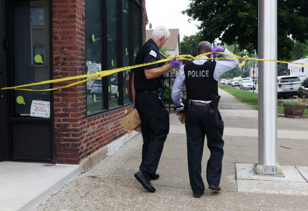 A police detective and evidence technician cross crime scene tape while investigating a multiple shooting in the 7100 block of South Woodlawn Avenue on July 4, 2024. (John J. Kim/Chicago Tribune)