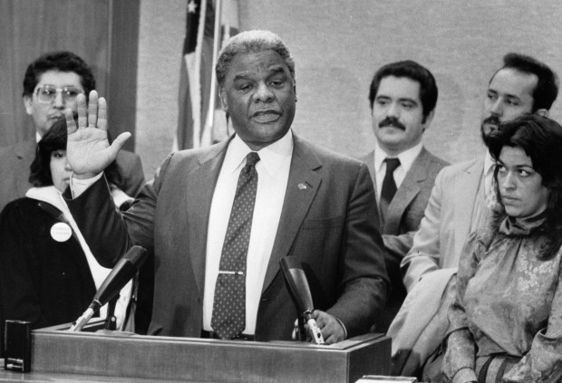 Mayor Harold Washington, center, raises his hand as he talks about signing an executive order to assure that all residents of Chicago, regardless of nationality or citizenship, shall have fair and equal access to municipal benefits, opportunities and services on March 7, 1985. With Washington is his Latino Advisory Commission, including Jesus "Chuy" Garcia, third from right in background. (Carl Hugare/Chicago Tribune)