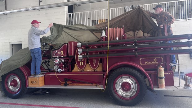 At the front of the fire truck is Old Number One Preservation Committee Chairman Bob Stadlman, being assisted in covering the 100-year-old restored firetruck by member Darrell Hughes at the Mundelein Fire Department on May 9, 2025. (Yadira Sanchez Olson/For the Lake County News-Sun)