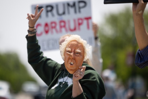 Julie Vahos holds a paper mâché Donald Trump mask that she made, called Trumpocchio, as people protest against supporters of Truth Trump Store, owned by Lisa Fleischmann, staying open about a half of a mile away from the store across the street on Saturday, May 31, 2025, in Huntley. (Audrey Richardson/Chicago Tribune)