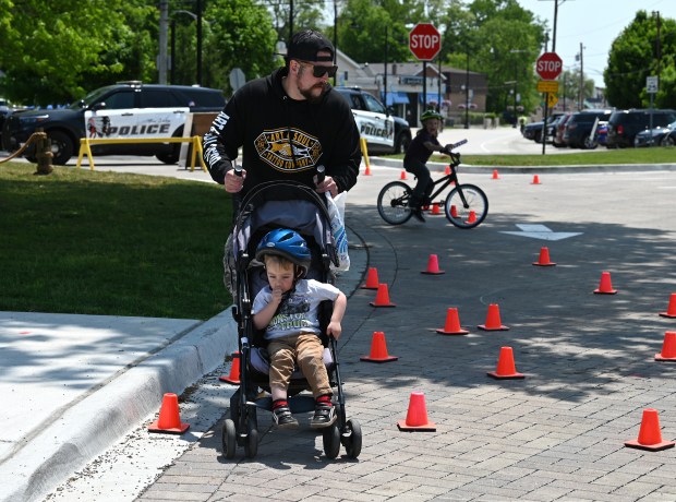 Trying out the safety cone bike rodeo challenge with a stroller is parent Justin Murov of Spring Grove who is pushing son Sullivan, 2, at the Grand Opening Beach Party and Bike Rodeo on May 31, 2025 at Lakefront Park in Fox Lake. (Karie Angell Luc/Lake County News-Sun)